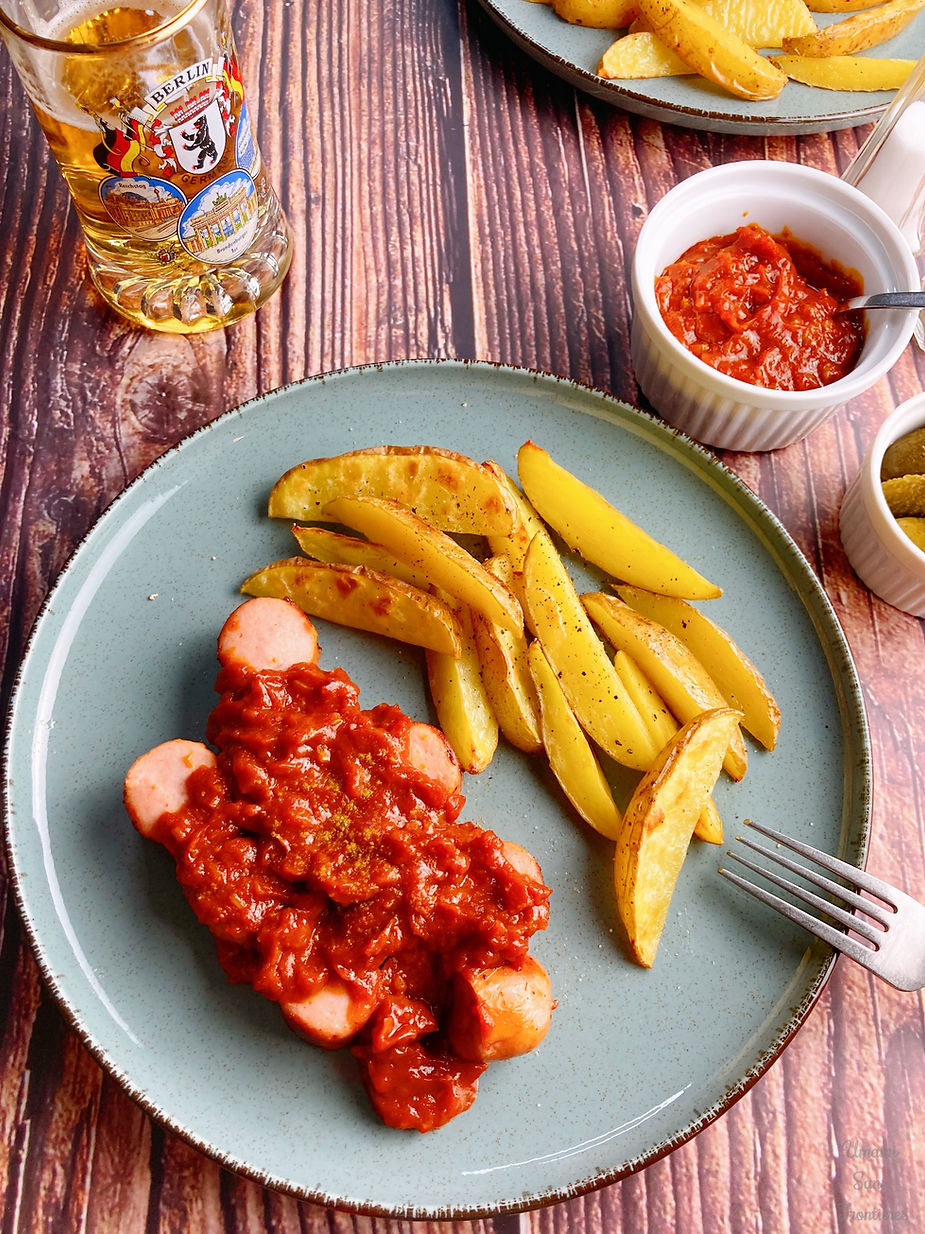 Grilled sausage, curry tomato sauce, french fries, pickles, beer and fork on a plate