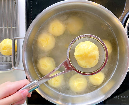 Hot water in a pot, potato dumplings, ladle for removing scum, left hand