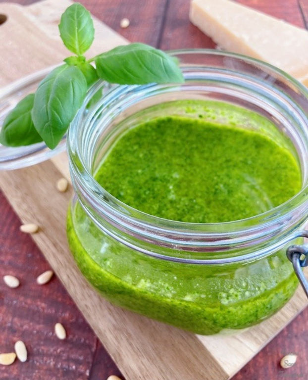 Genovese sauce (basil sauce) in a glass container, basil leaves, pine nuts, wooden board, parmesan cheese