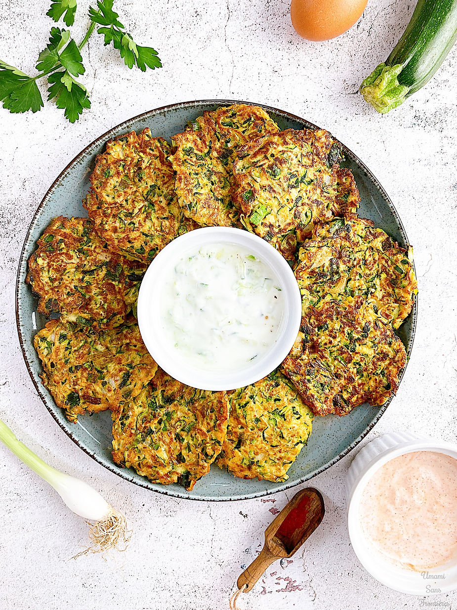 Mujebel on a plate, zucchini fritters, yogurt sauce in a bowl, onion, zucchini, parsley, egg, paprika powder