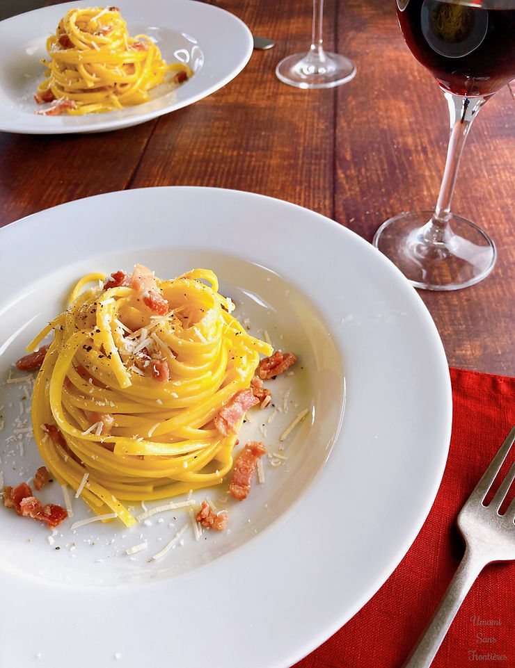 Carbonara on a plate, bacon, cheese, black pepper, wine glass with red wine, fork and red table napkin