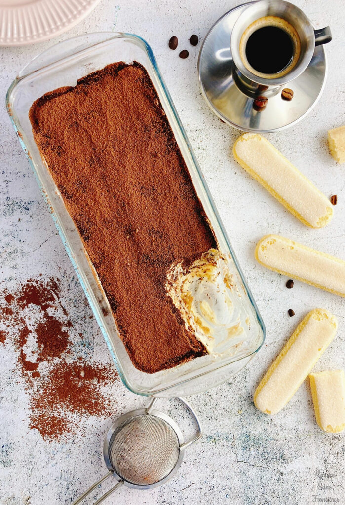 Tiramisu, biscotti savoiardi, espresso and tea strainer in a glass plate