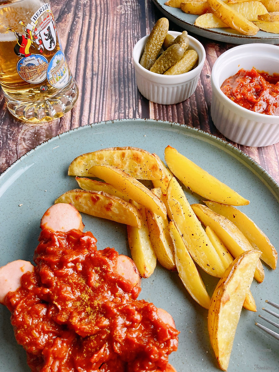 Grilled sausage, curry tomato sauce, french fries, pickles, beer and fork on a plate