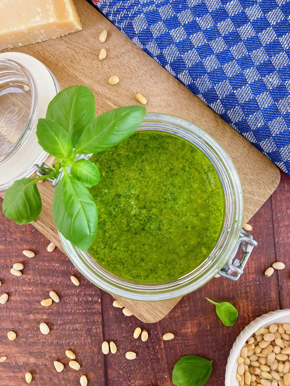 Genovese sauce (basil sauce) in a glass container, basil leaves, pine nuts, wooden board, dish towel