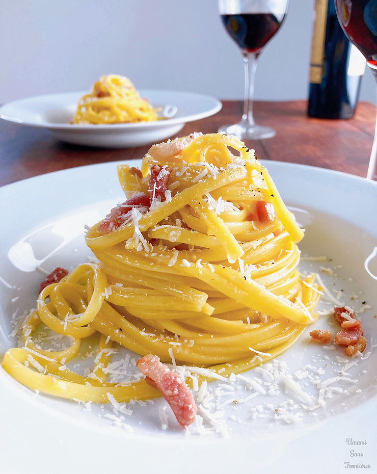 Carbonara on a plate, bacon, parmesan cheese, black pepper, red wine in a wine glass, wine bottle