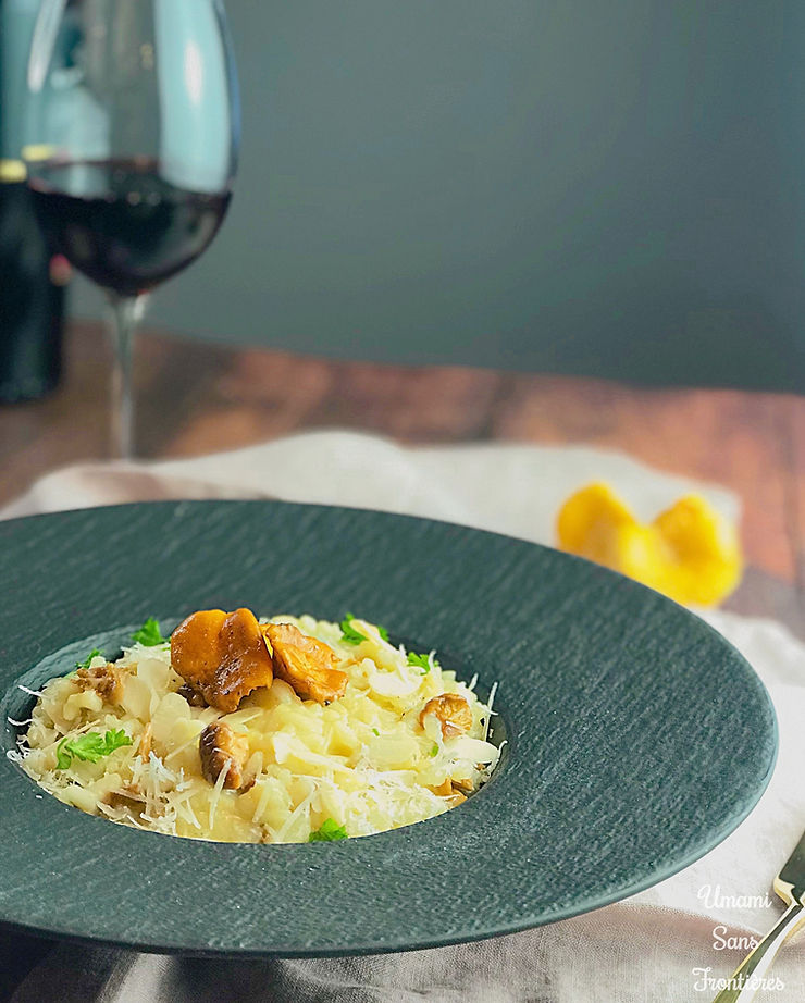 Wine bottle, red wine, wine glass, mushrooms (chanterelle), mushroom cheese risotto on a plate, fork, cloth