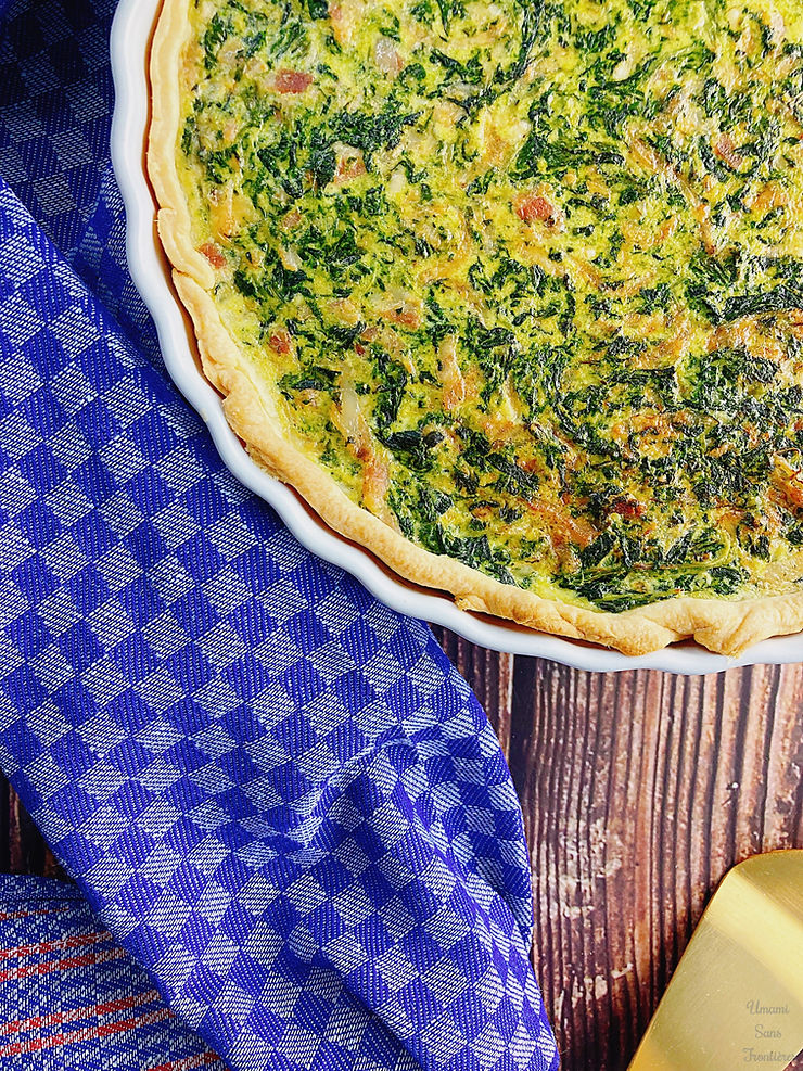 Spinach and bacon quiche in a heat-resistant dish, kitchen cloth, and cake server