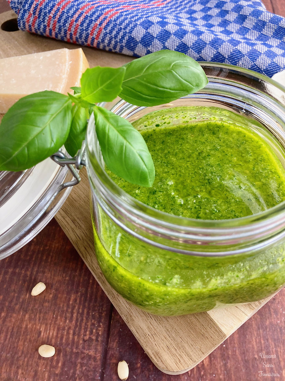 Genovese sauce in a glass container, basil leaves, parmesan cheese, pine nuts, wooden board and dish towel