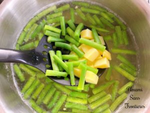 Pasta Pesto potatoes green beans and a slotted spoon in a hot water in a pot