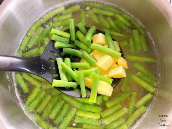 Pasta Pesto potatoes green beans and a slotted spoon in a hot water in a pot