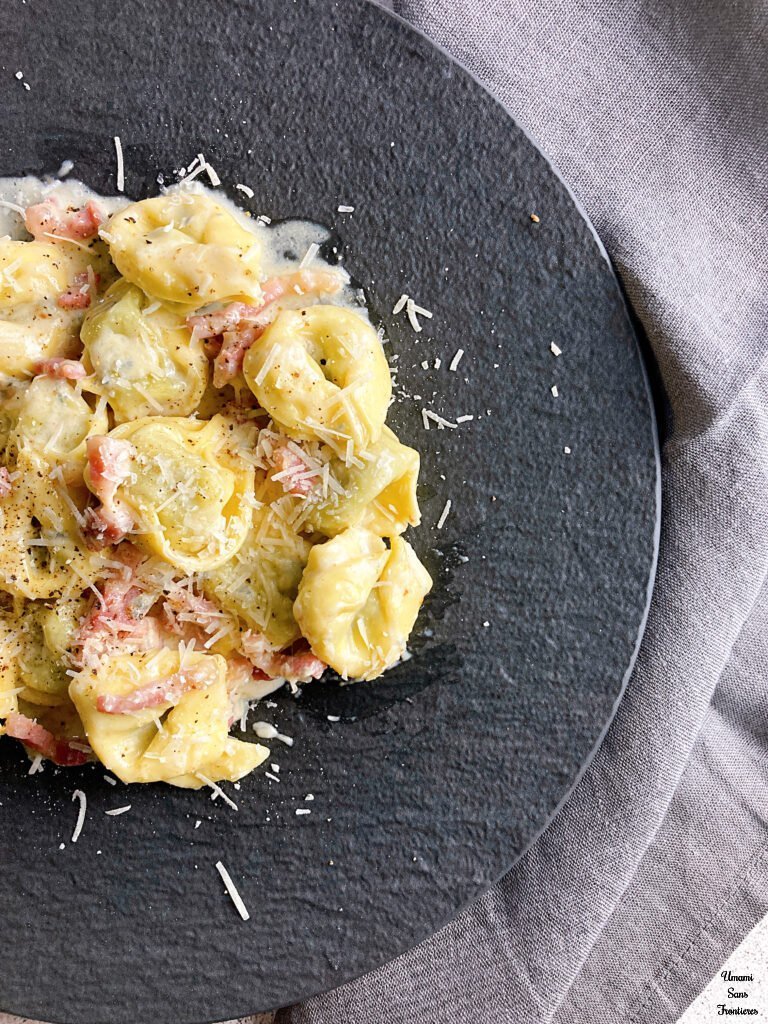 Tortellini with Bacon and Gorgonzola Cream Sauce on a black plate grey table napkin