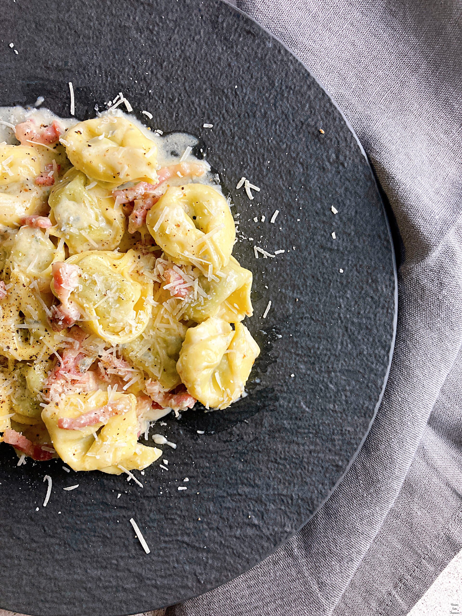 Tortellini with Bacon and Gorgonzola Cream Sauce on a black plate grey table napkin