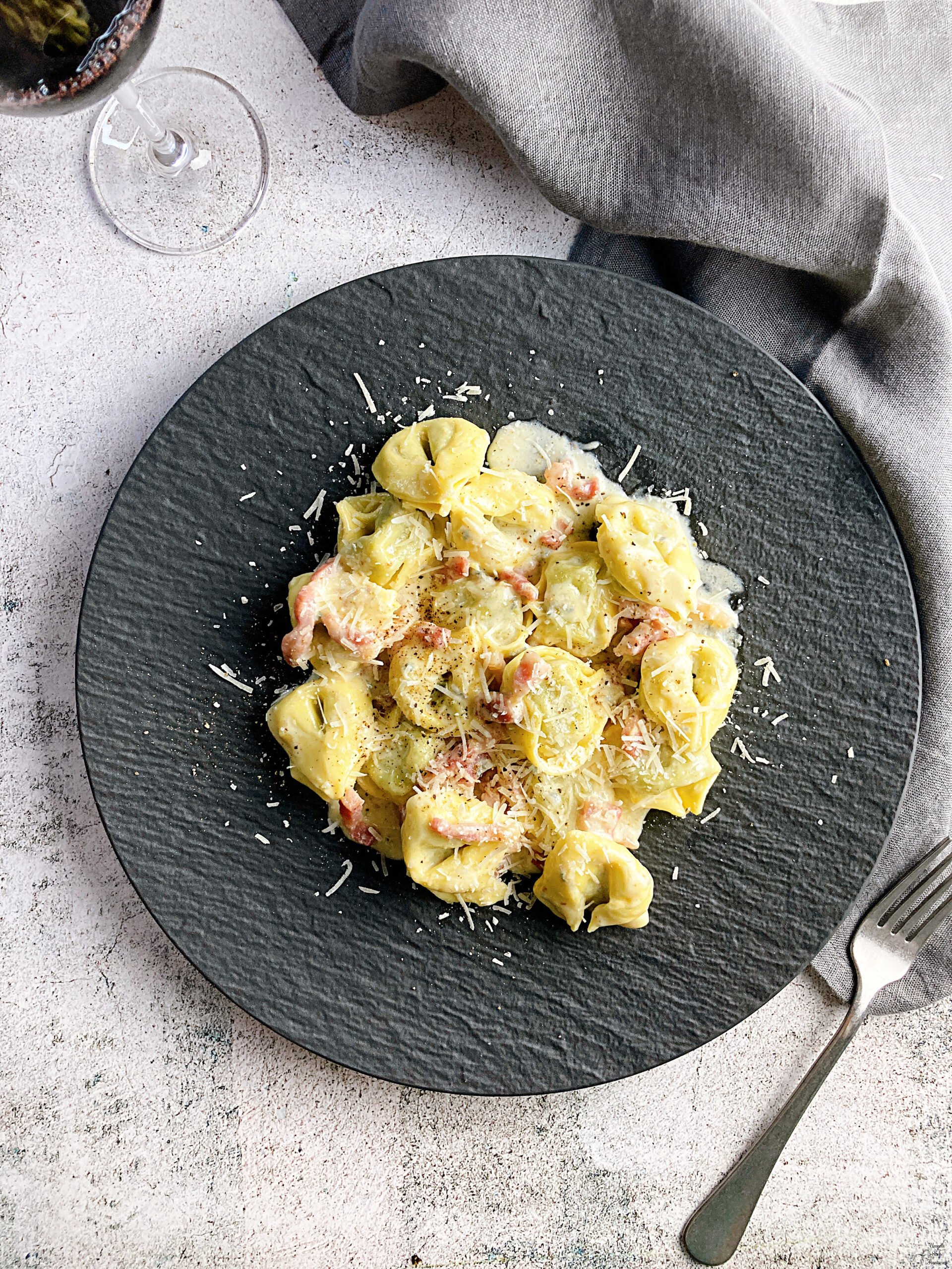 Tortellini with Bacon and Gorgonzola Cream Sauce grey table napkin folk red wine wine glass