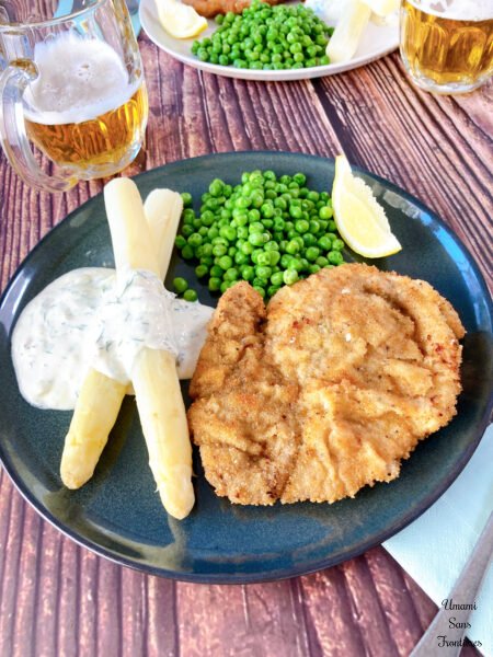 Schnitzel green peas asparagus yogurt sauce lemon on the blue dish beer